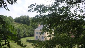 A house with a light-colored facade, surrounded by lush greenery and trees.