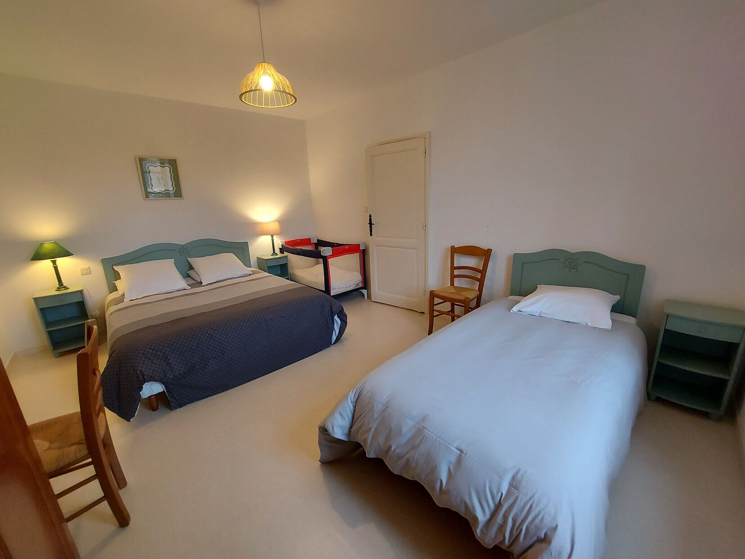 A room with two beds, a chair, a desk, and a hanging light fixture.
