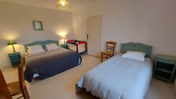 A room with two beds, a chair, a desk, and a hanging light fixture.