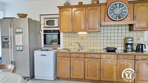 Une cuisine avec des meubles de rangement en bois, un four à micro-ondes encastré, une machine à café et une horloge.