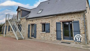 Un bâtiment en pierre avec un toit recouvert de tuiles grises, un escalier en métal et un logo indiquant qu’il s’agit d’un établissement affilié à Gîtes de France.