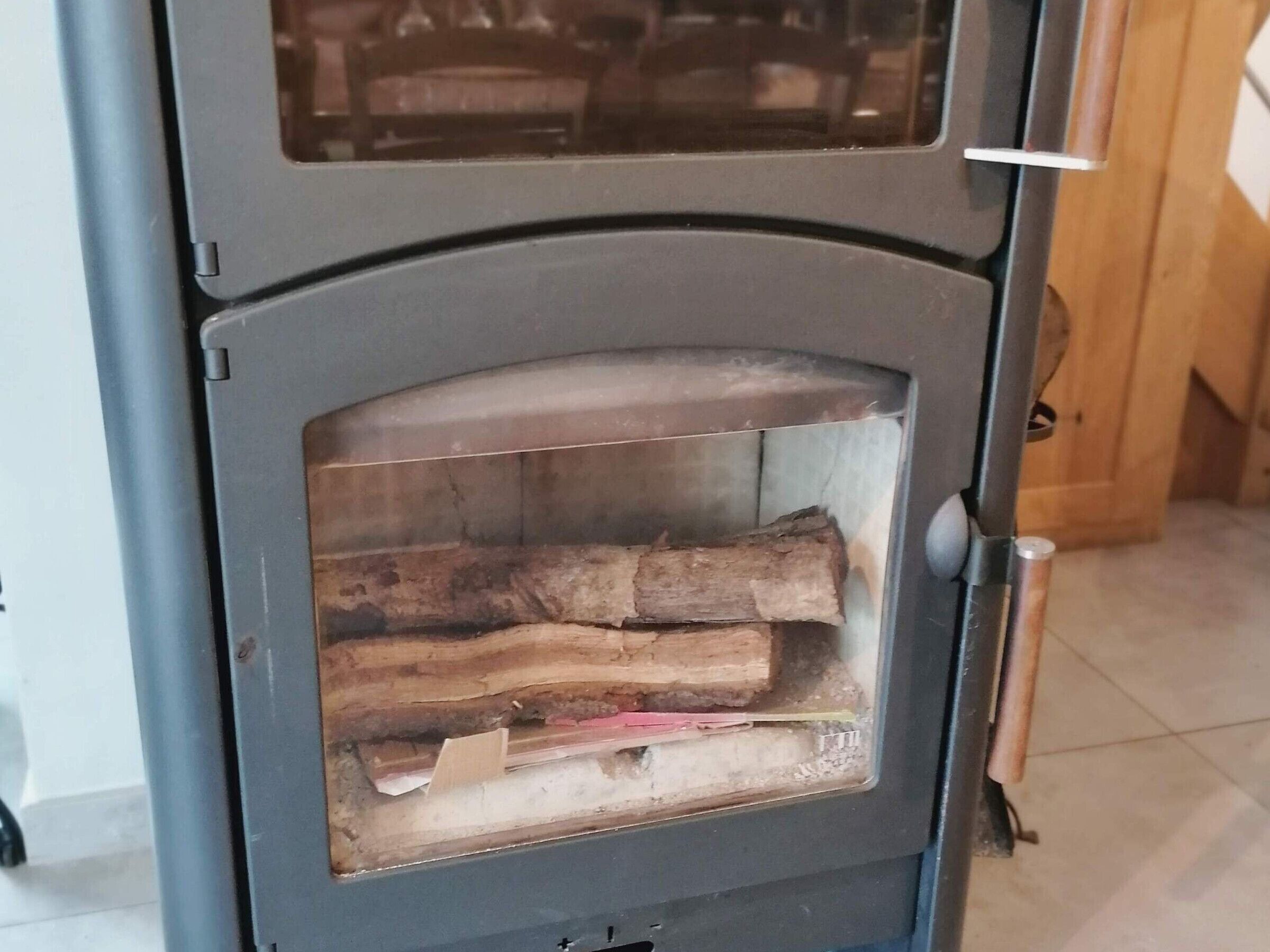 Un poêle à bois doté d’une porte en verre, d’une poignée en métal et d’une bûche visible à l’intérieur.