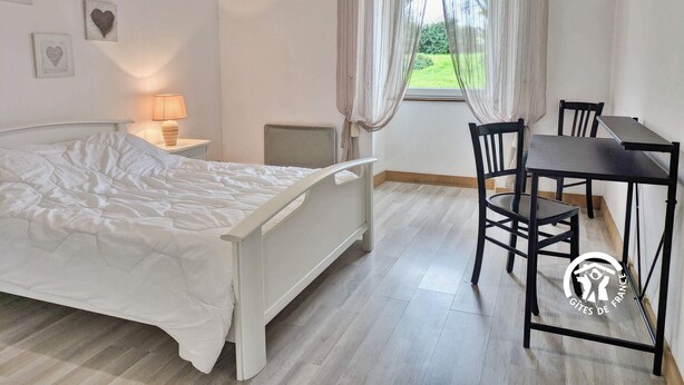 Une chambre à coucher avec un lit, une table de chevet, une lampe, une fenêtre avec des rideaux et une vue sur la verdure à l’extérieur.