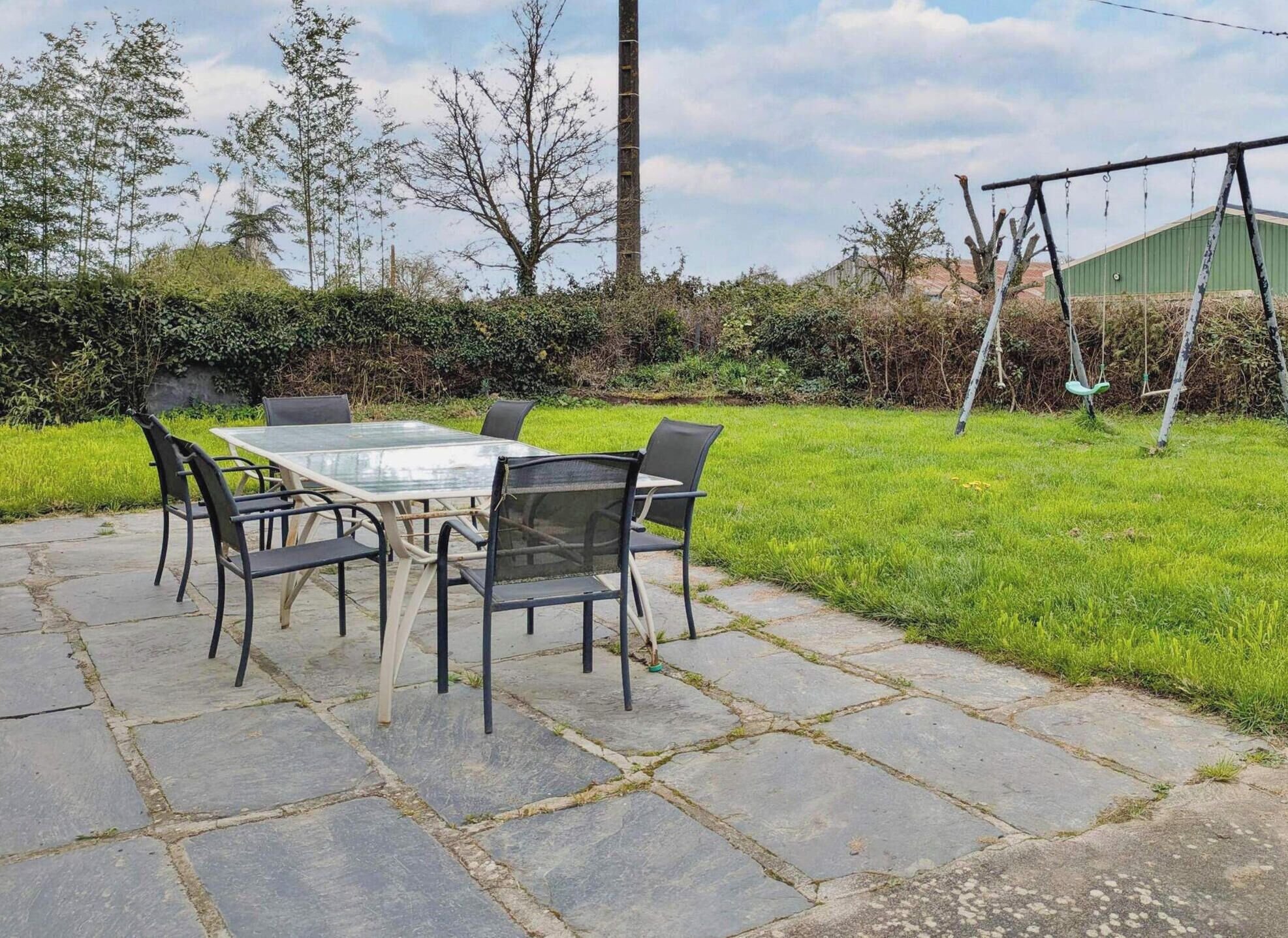 An outdoor patio with a table and chairs, surrounded by a grassy area and a swing set.