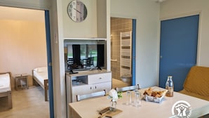 Une chambre d’hôtel compacte comprenant un lit, un bureau avec un ordinateur, une petite table avec un vase et des verres, et une horloge au mur.