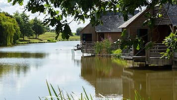A rustic wooden cabin with a dock extending into a calm lake, surrounded by lush greenery and trees.