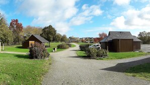 Un chemin de gravier mène à une rangée de bâtiments en bois, qui semblent être un terrain de camping ou un centre de loisirs. Le ciel est dégagé et le feuillage automnal forme un décor en arrière-plan.