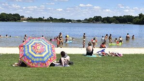 A lakeside scene with people swimming and sunbathing.