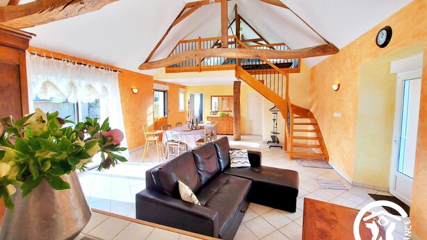 A spacious living area with a high ceiling, wooden beams, a staircase, and a dining area.