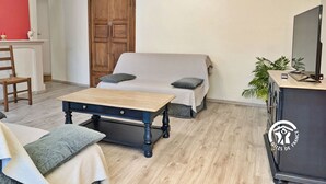A furnished room with a wooden table, a sofa, a cabinet with a TV, and a red wall. - Charming Countryside Retreat with Farm Experience and Nearby Forest (L'Huisserie)