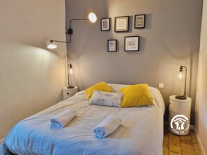 A neatly made bed with two rolled towels, two bedside lamps, and a wall with framed inspirational quotes. - Charming Lakeside Manor with Garden, Ping-Pong, Biking, and Fishing (Cossé-le-Vivien)