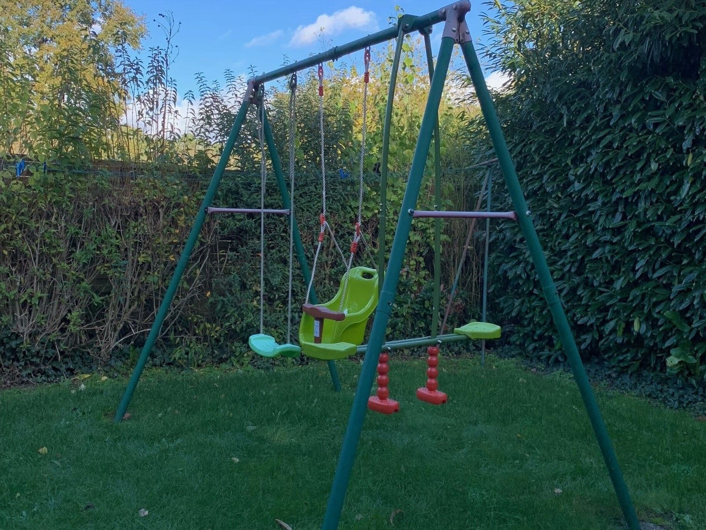 A swing set in a garden with a hedge in the background.