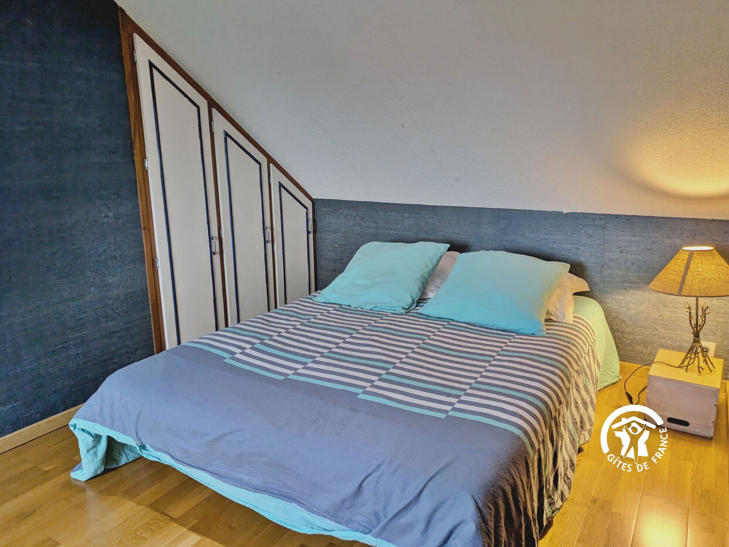 Une chambre à coucher avec un lit, deux oreillers, une table de chevet avec une lampe et une armoire.