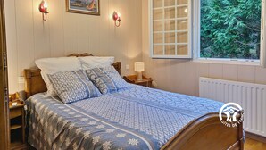 Un dormitorio con cama de madera, mesita de noche, lámpara, ventana con vista a árboles y un cuadro en la pared.