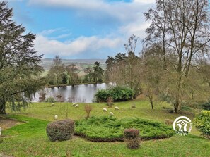 A serene landscape with a lake, sheep grazing, and a logo in the corner. - Charming Lakeside Cottage with Fishing, Hiking, and Family Activities (Saint-Pierre-sur-Orthe)