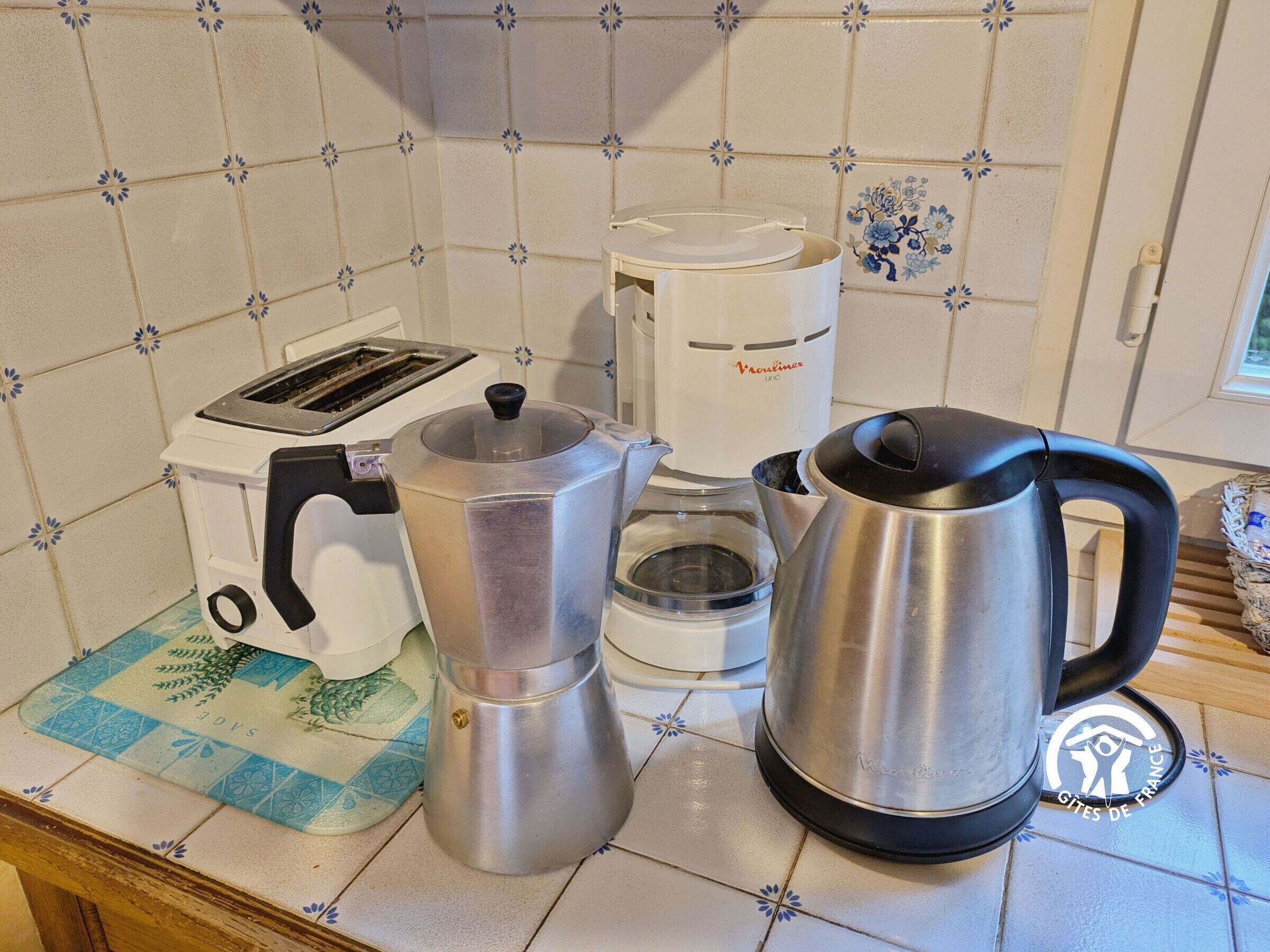 A kitchen counter with a coffee maker, a kettle, a toaster, and a French press.