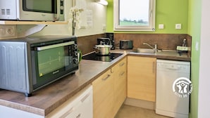 A compact kitchen with a microwave, oven, and dishwasher. There is a window with a view of the outdoors. - "Charming Lakeside Chalet with Private Fishing Pier, Game Room, and Nearby Village Amenities" (Villiers-Charlemagne)
