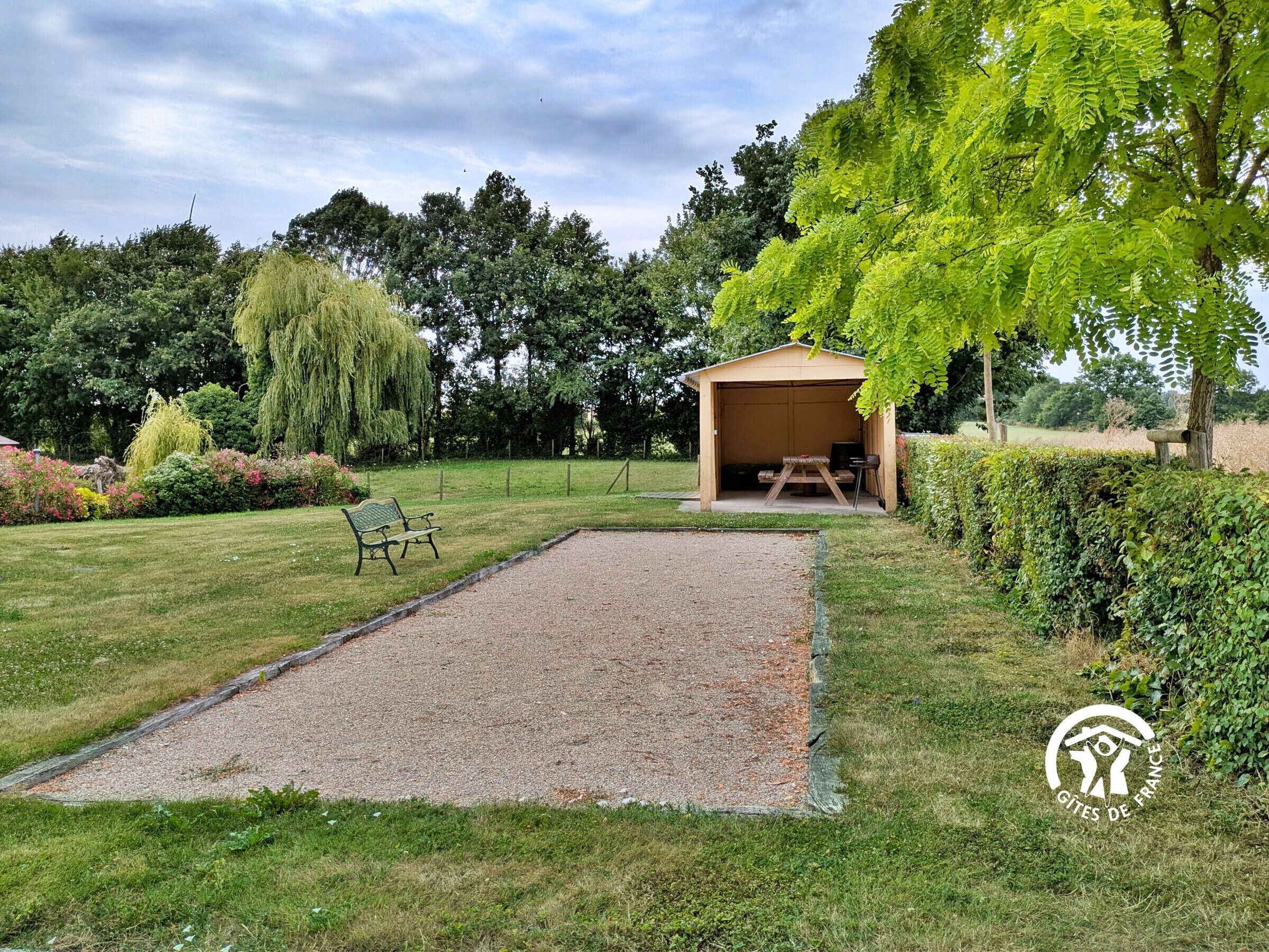 Un espacio al aire libre techado con un sendero de grava, un banco y una mesa de picnic.