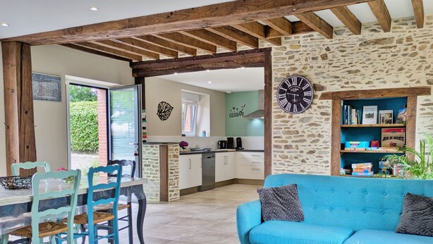 A modern kitchen with stone walls, a dining area with a table and chairs, and a blue sofa with cushions. - Cottage Nature & Comfort, 6 Pers., Accessible, Garden, Outdoor Games (Cossé-le-Vivien)