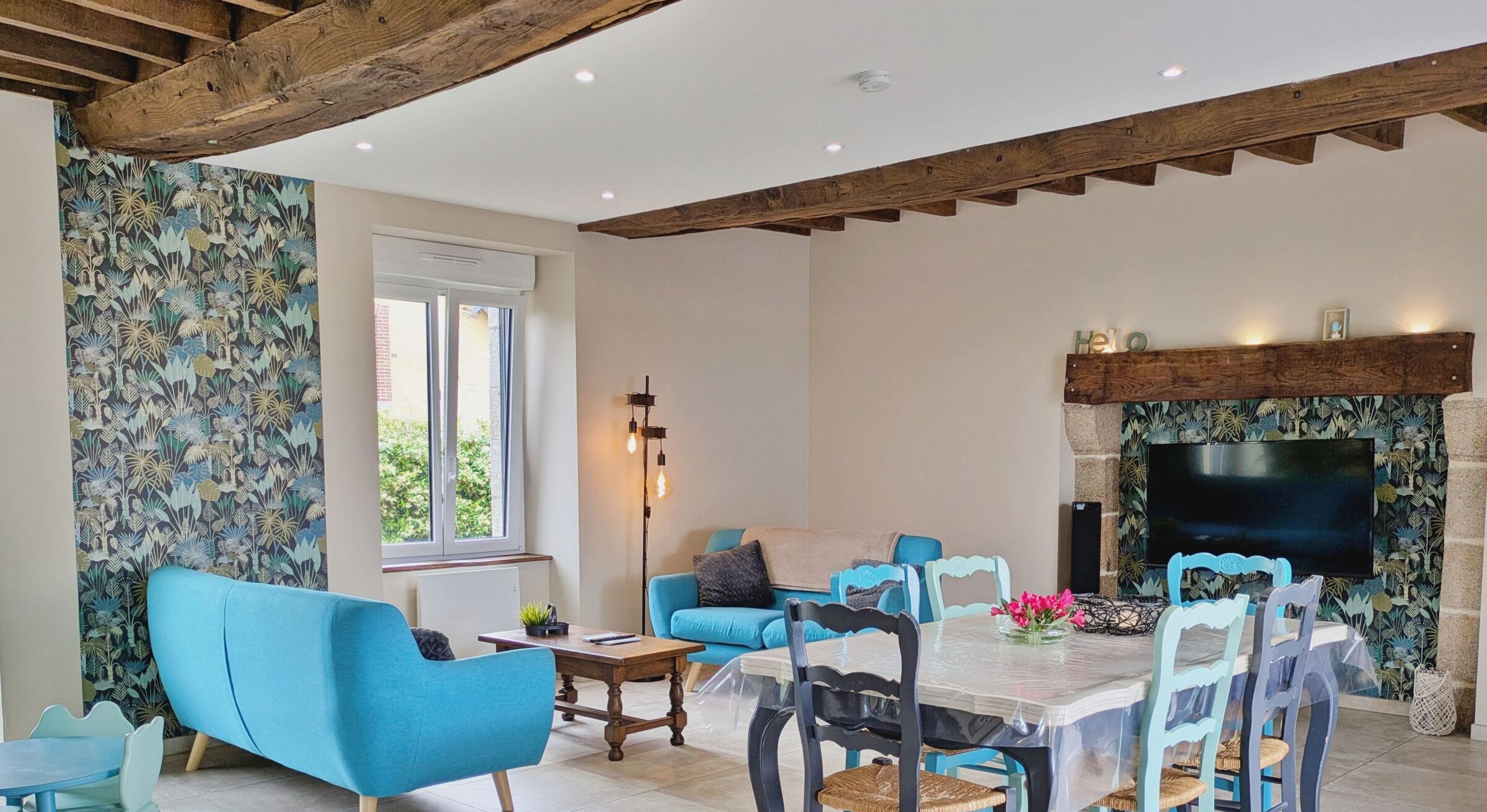 Un ampio soggiorno con soffitto alto, camino, televisione e zona pranzo con sedie blu e tavolo.