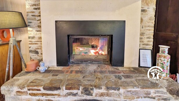 A stone fireplace with a fire, a lamp, and a teapot on a table.