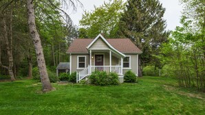 A single-story house with a front porch, surrounded by a grassy yard and trees.