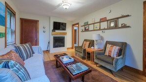 A living room with a sofa, armchair, coffee table, fireplace, television, and shelves with framed pictures.