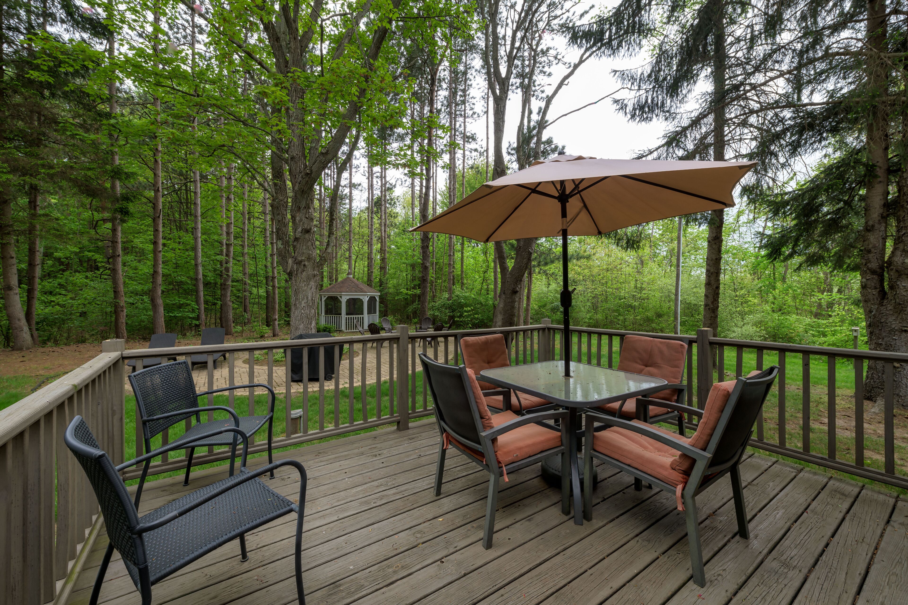 A deck with a glass table and chairs, an umbrella, and a small gazebo.