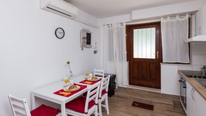 Cocina compacta con armarios blancos, una puerta de madera y un comedor con mesa blanca y sillas rojas.