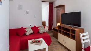 Un espacio habitable pequeño con un sofá rojo, un televisor y una mesita con una bandeja.