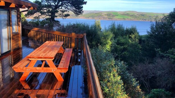 En träaltan med ett picknickbord, med utsikt över en sjö och skogbeklädda kullar.