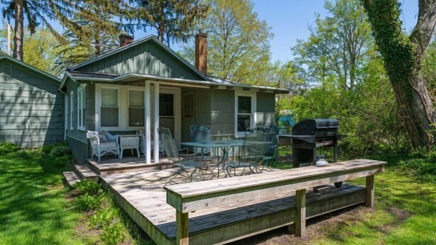 Ein kleines Haus mit Veranda, einem Tisch mit Stühlen und einem Grill.