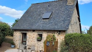 A stone house with a sloped roof, a small window, and a door. There is a solar panel on the roof, a wooden fence, and a sign that reads "Cottage." - Cozy Stone Cottage with Private 8ha Fishing Pond and Scenic Surroundings - Ideal for Nature Lovers (Alexain)