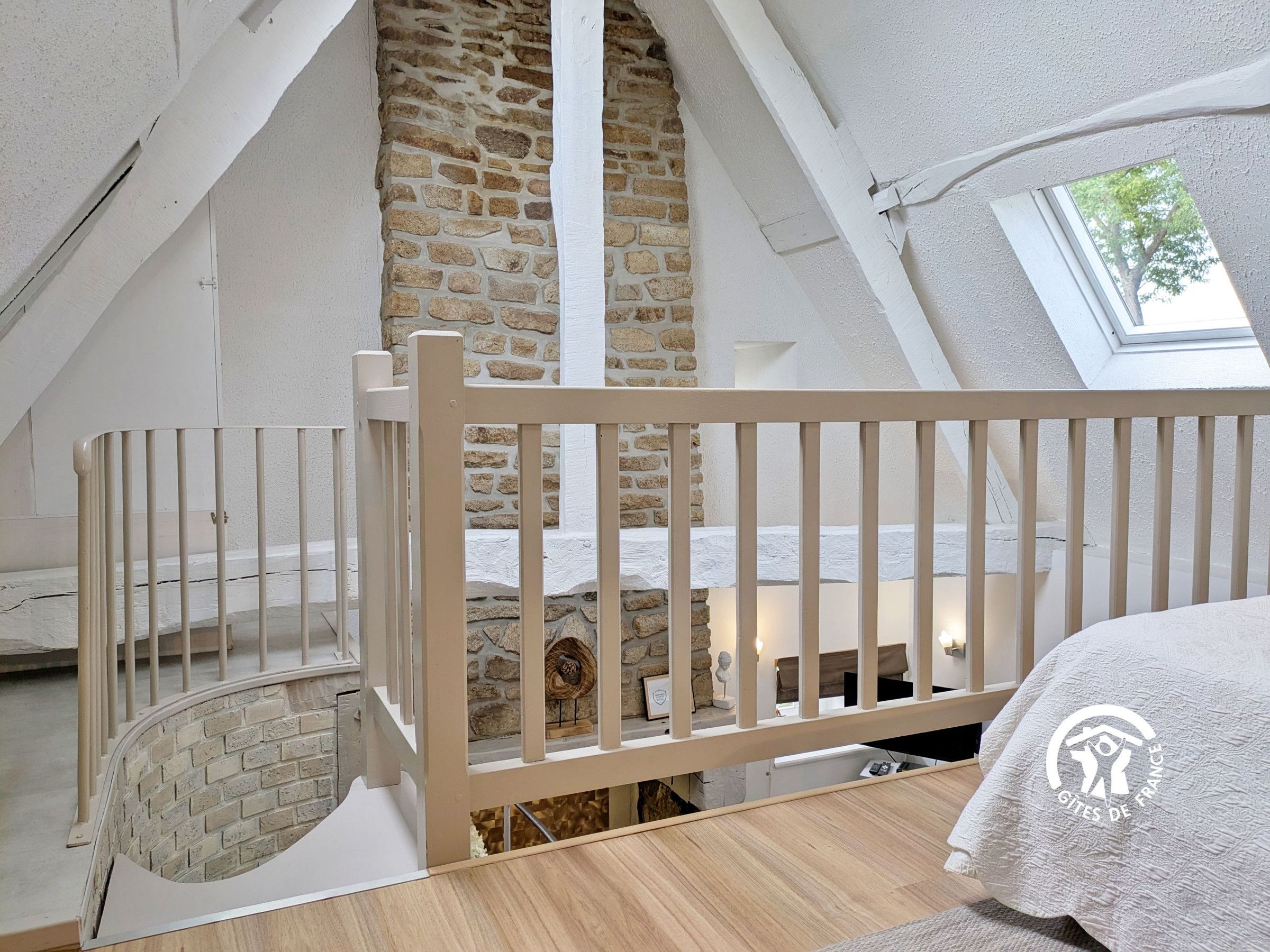A bedroom with a sloped ceiling, a stone wall, a wooden crib, and a skylight.