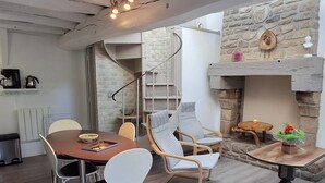 A modern kitchen with a stone wall, a built-in oven, and a dining area with a wooden table and chairs. - Cozy Stone Cottage with Private 8ha Fishing Pond and Scenic Surroundings - Ideal for Nature Lovers (Alexain)
