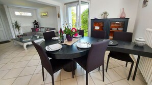 A dining area with a round table set for four, surrounded by chairs. There is a cabinet with glass doors to the right, and a radiator on the wall. - Charming 4-Bed House with Garden, 10min from Laval, Ideal for Families and Professionals (Courbeveille)