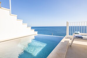 A clear blue sky, a white staircase leading to a infinity pool, and a white railing overlooking the ocean.