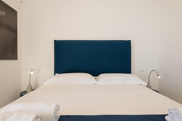 A neatly made bed with white linens, a dark blue headboard, and two bedside lamps.