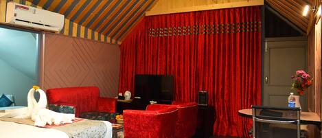 A hotel room with a bed, red velvet sofa, a flat-screen TV, and a small table with a vase of flowers.