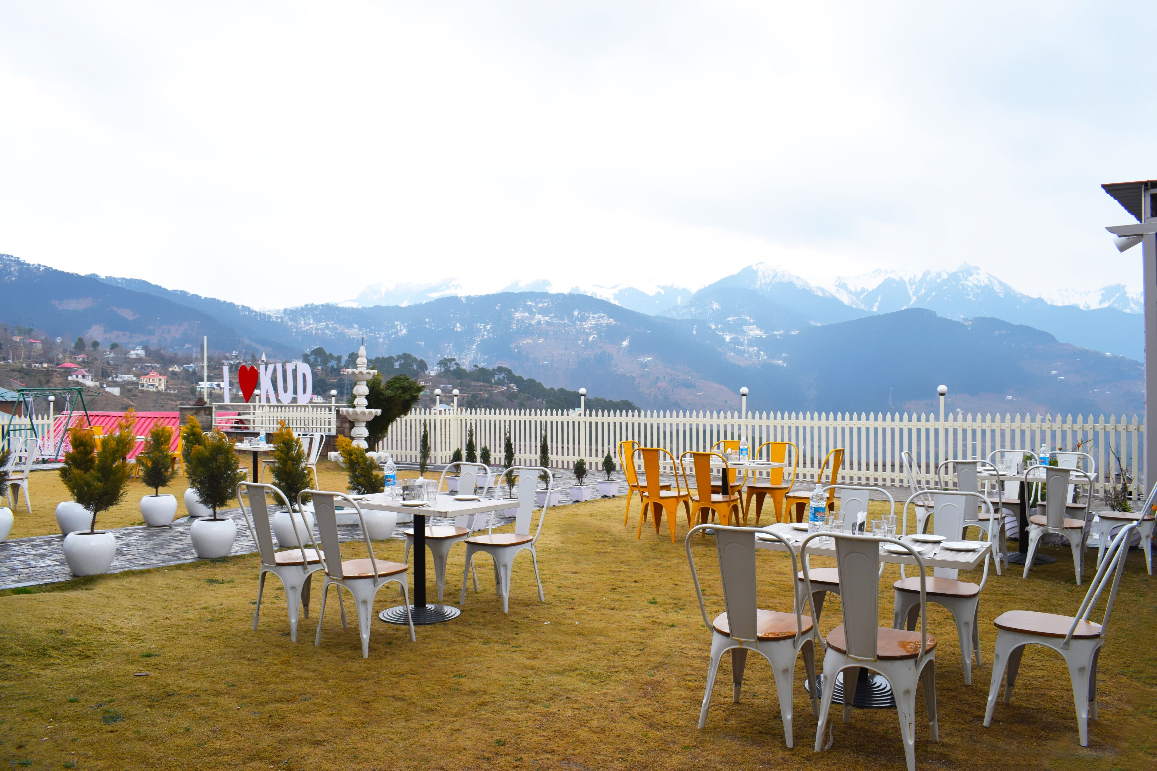 An outdoor dining area with tables and chairs, a white fence, and a mountainous backdrop.