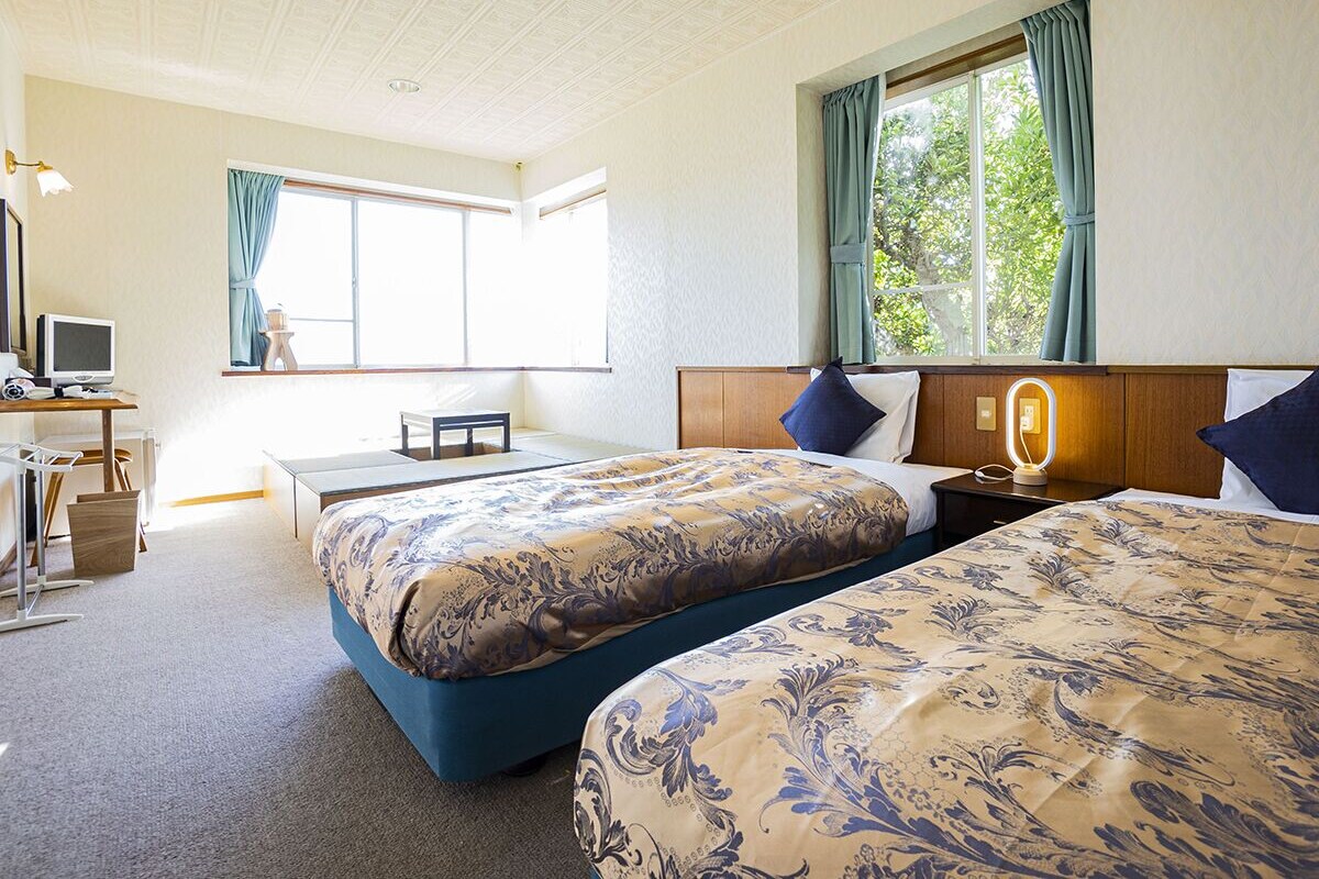 A hotel room with two beds, a desk, a chair, a TV, and a window with curtains.