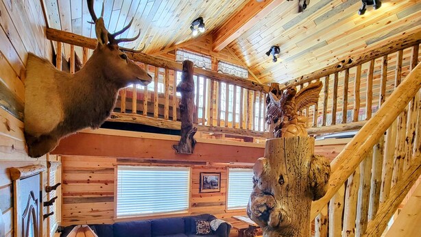 A log cabin interior with a deer head mounted on the wall, a wooden staircase, a blue sofa, and a fireplace. - 15 min to Yellowstone. Newly built in 2018 this cabin is meticulous . WIFI ÷ AC (Island Park)