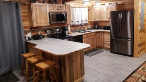 A wooden cabin-style kitchen with a large island, bar stools, a refrigerator, a microwave, and a coffee maker. - 15 min to Yellowstone. Newly built in 2018 this cabin is meticulous . WIFI ÷ AC (Island Park)