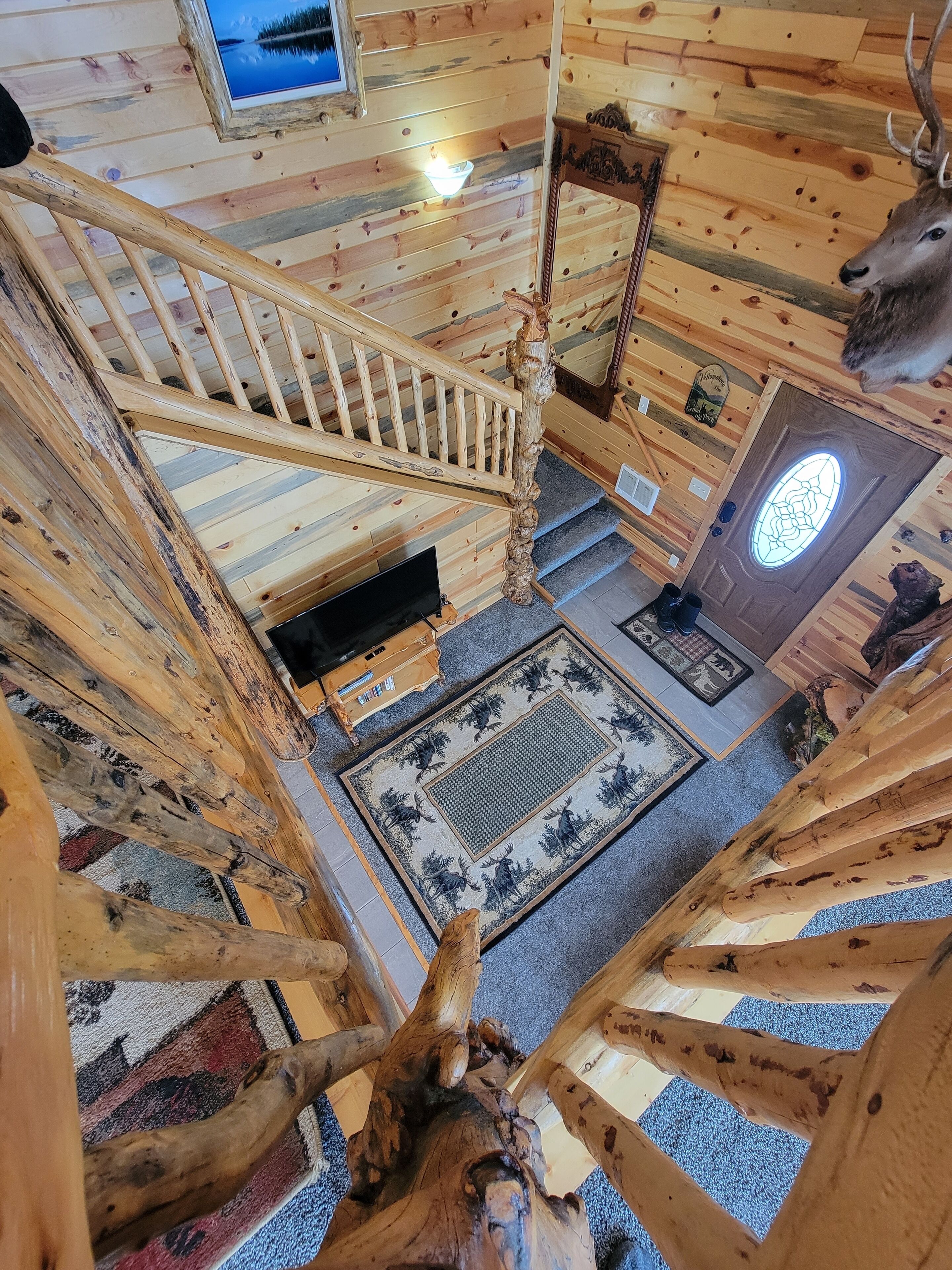 L’intérieur d’un chalet en bois, avec un escalier, une tête de cerf et un poisson, tous les trois fixés au mur.