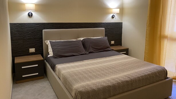 Une chambre à coucher avec un lit, deux tables de chevet et des lampes fixées au mur.
