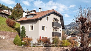 Ein zweistöckiges Haus mit einem geneigten Dach, einer Steintreppe und Blick auf Berge im Hintergrund.