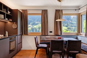 Una cocina moderna con comedor, ventanas amplias con cortinas y vistas a un paisaje boscoso.