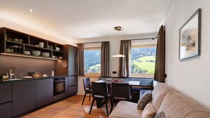 Eine moderne Küche mit Essbereich, einer Couch und Blick auf eine grüne Landschaft.