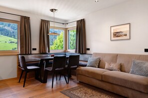 Une pièce comprenant une table à manger, des chaises, un canapé, un tapis et une fenêtre avec des rideaux.