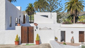 A white building with a wooden door, potted plants, and a clear blue sky. - Holiday Home ‘Maria Dolores’ with Mountain View, Wi-Fi, Garden & Terrace (HARIA)